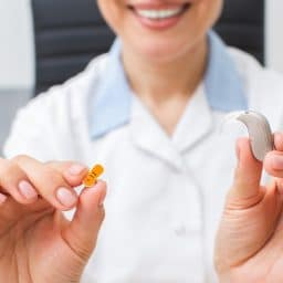 Audiologist holding hearing aid and battery in her hands.