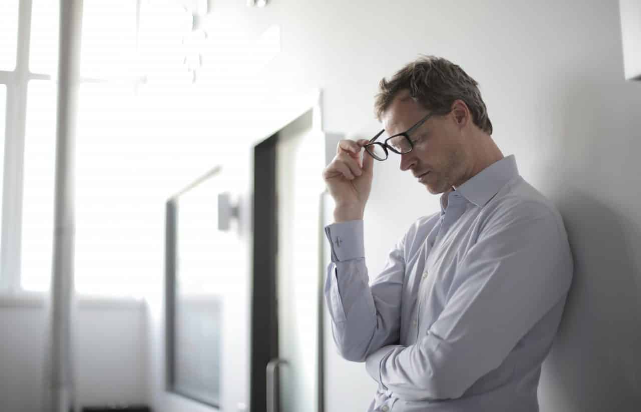 Younger man looking stressed and resting against a wall.