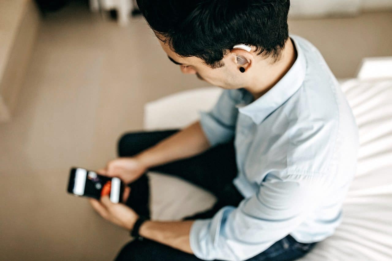 Young businessman with a hearing aid looking at his smartphone.