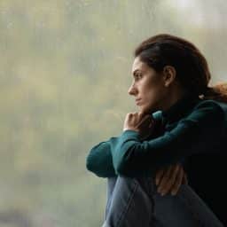 Side view of a morose woman looking out rainy window
