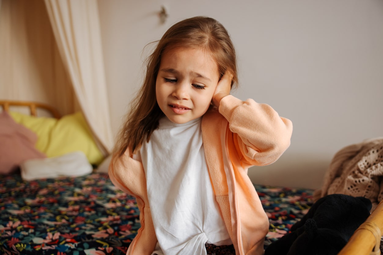 Young girl holds ear in pain