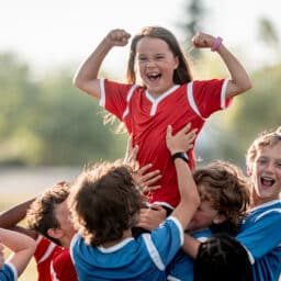 A team of kids in jerseys hold up a fellow player in celebration.