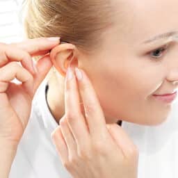 Young woman puts on her new hearing aid.
