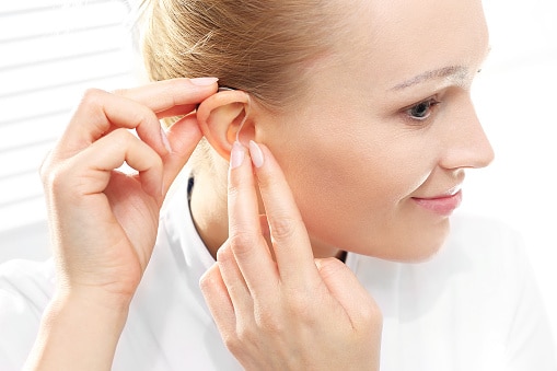 Young woman puts on her new hearing aid.