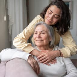 Daughter hugging her senior mother on her couch.