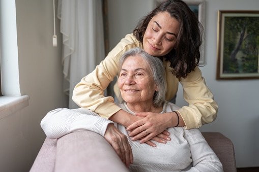 Daughter hugging her senior mother on her couch.
